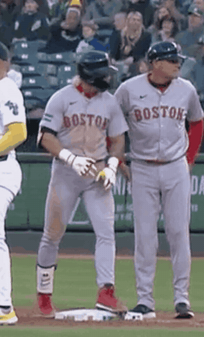 A Couple Of Baseball Players Are Standing On A Field . One Of The Players Is Wearing A Boston Jersey . GIF