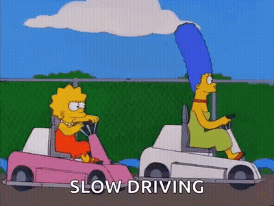 A Couple Of Cartoon Characters Are Driving Golf Carts And The Words Slow Driving Are Visible . GIF