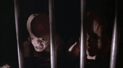 A Couple Of Creepy Dolls Are Behind Bars In A Dark Room GIF