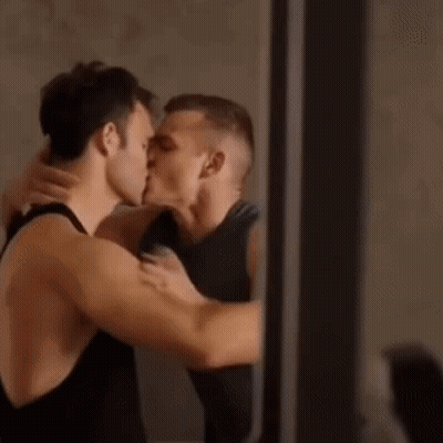 A Couple Of Men Are Kissing Each Other In Front Of A Mirror . GIF