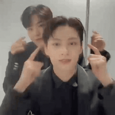 A Couple Of Men Are Standing Next To Each Other And Making Funny Faces With Their Fingers . GIF