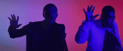 A Couple Of Men Are Standing Next To Each Other In A Dark Room With Their Hands Up In The Air . GIF