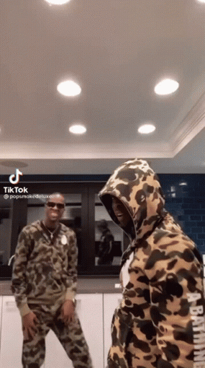 A Couple Of Men Are Standing Next To Each Other In A Kitchen Wearing Camouflage Hoodies . GIF