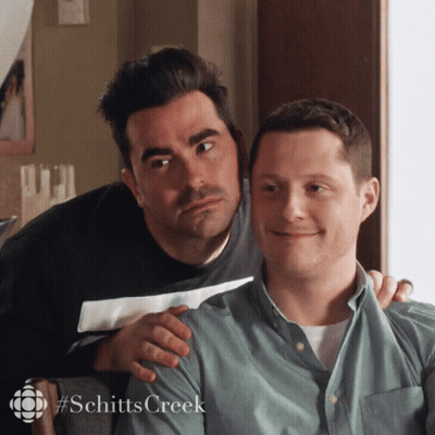 A Couple Of Men Sitting Next To Each Other With The Word Schitts Creek On The Bottom GIF