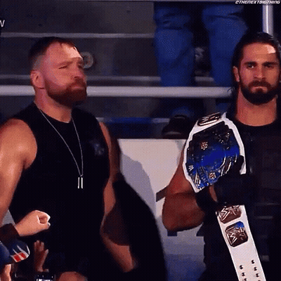 A Couple Of Men Standing Next To Each Other In A Stadium . One Of The Men Is Wearing A Championship Belt . GIF