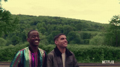 A Couple Of Men Standing Next To Each Other With A Netflix Logo Behind Them GIF