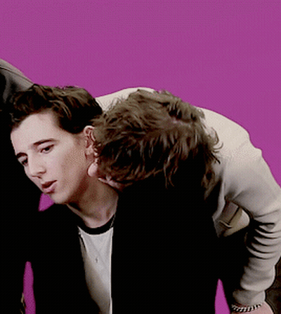 A Couple Of Men Standing Next To Each Other With A Pink Background GIF