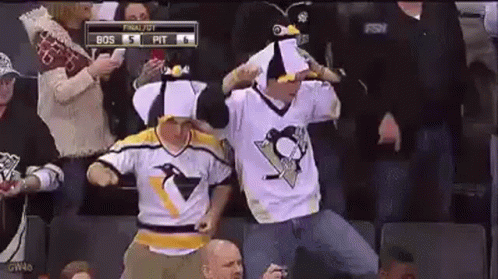 A Couple Of Men Wearing Penguin Jerseys Are Dancing In The Stands During A Hockey Game . GIF