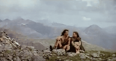 A Couple Of People Are Sitting On Top Of A Rocky Mountain . GIF