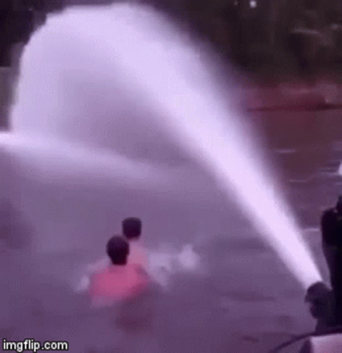 A Couple Of People Are Standing In Front Of A Water Fountain . GIF