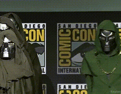 A Couple Of People Standing In Front Of Comic Con Posters GIF
