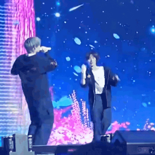 A Couple Of People Standing On A Stage Holding Microphones GIF