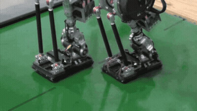 A Couple Of Robots Standing On A Green Surface GIF