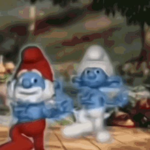 A Couple Of Smurfs Are Standing Next To Each Other On A Table GIF