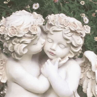 A Couple Of Statues Of Cherubs Kissing Each Other In A Garden . GIF
