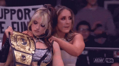 A Couple Of Women Are Standing Next To Each Other In A Ring Holding A Wrestling Championship Belt . GIF