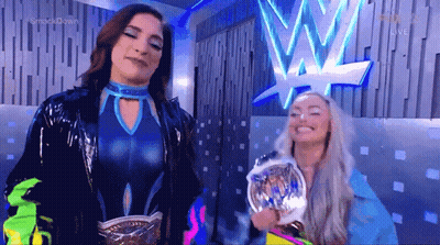 A Couple Of Women Are Standing Next To Each Other In Front Of A Wrestling Logo . GIF