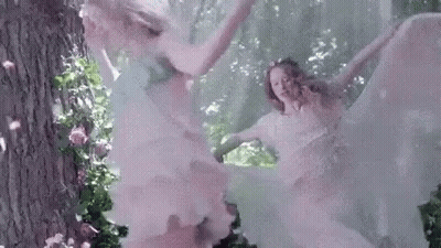 A Couple Of Women In White Dresses Are Dancing In The Woods . GIF