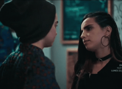 A Couple Of Women Looking At Each Other In A Dark Room With A Sign That Says Lucky 7 GIF