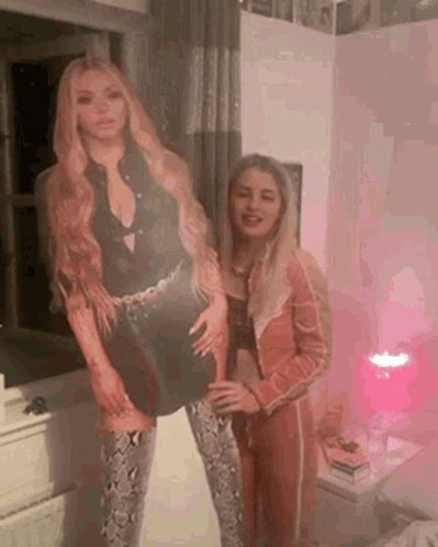 A Couple Of Women Standing Next To Each Other In A Room . GIF