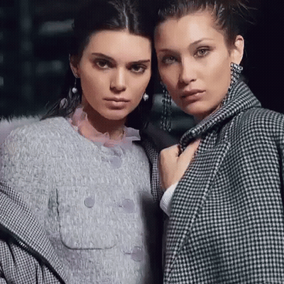 A Couple Of Women Standing Next To Each Other Wearing Coats And Earrings . GIF