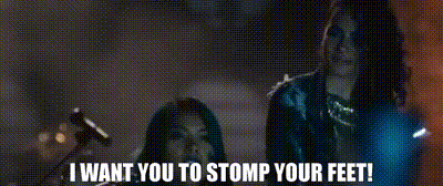 A Couple Of Women Standing Next To Each Other With The Words `` I Want You To Stomp Your Feet '' Written On The Screen . GIF