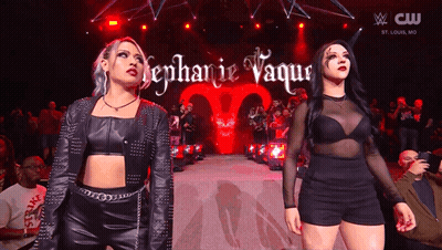 A Couple Of Women Standing On A Stage With The Name Stephanie Vaquer On The Screen GIF