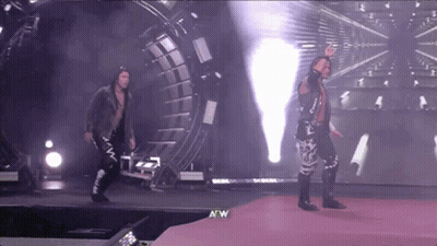 A Couple Of Wrestlers Are Walking On A Stage With A W Logo In The Corner GIF