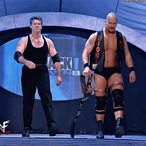 A Couple Of Wrestlers Standing Next To Each Other Holding A Belt GIF