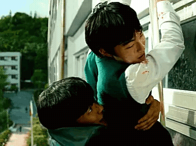 A Couple Of Young Men Are Hugging Each Other In Front Of A Window . GIF