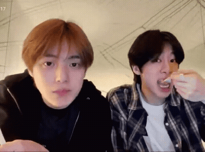 A Couple Of Young Men Are Sitting Next To Each Other And Eating Food . GIF