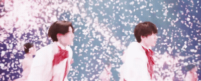 A Couple Of Young Men Are Standing In Front Of A Wall Of Cherry Blossoms . GIF