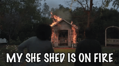 A Couple Standing In Front Of A Burning Shed With The Words My She Shed Is On Fire GIF