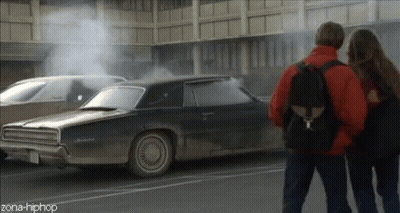 A Couple Standing Next To A Car That Has Smoke Coming Out Of It And The Words Zona-Hiphop On The Bottom GIF