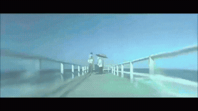 A Couple Walking On A Pier With Umbrellas GIF