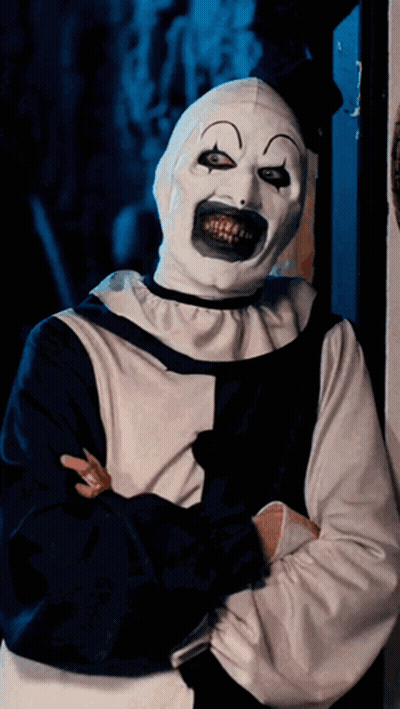 A Creepy Clown With A Huge Smile On His Face Is Standing With His Arms Crossed GIF