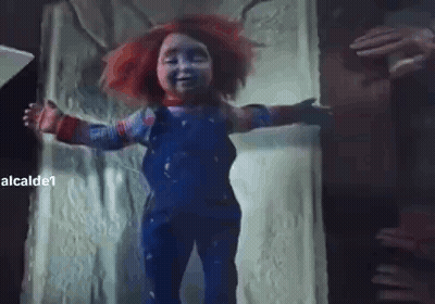 A Creepy Doll With Red Hair And Blue Overalls Is Standing In A Doorway With Its Arms Outstretched . GIF
