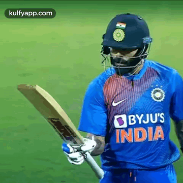A Cricket Player Is Wearing A Helmet And Holding A Bat On A Field . GIF