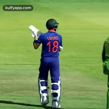 A Cricket Player Wearing A Blue Jersey With The Number 18 On It Is Standing On A Field Holding A Bat . GIF
