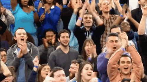 A Crowd Of People Applauding And Cheering With Their Hands In The Air GIF