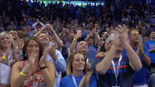 A Crowd Of People Are Applauding In Front Of A Sign That Says Team Partners GIF