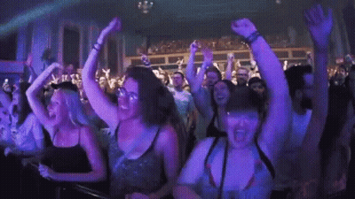 A Crowd Of People Are Dancing In A Club With Their Hands In The Air . GIF