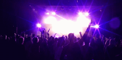 A Crowd Of People Are Dancing In Front Of A Stage With Purple Lights GIF