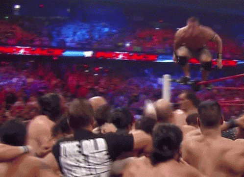 A Crowd Of People Are Gathered Around A Wrestling Ring With A Man Kneeling On A Rope GIF