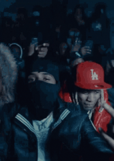 A Crowd Of People Are Gathered In A Dark Room And One Man Is Wearing A Red Jacket With A Ny Logo On It GIF