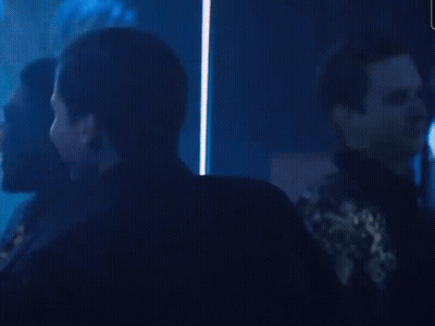A Crowd Of People Are Gathered In A Dark Room And One Of Them Is Holding A Coca Cola Glass GIF