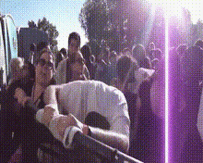 A Crowd Of People Are Gathered In A Park And A Purple Light Is Shining On Them GIF