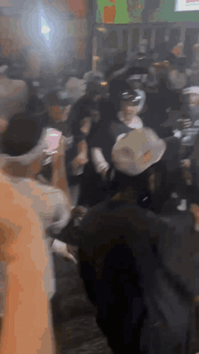 A Crowd Of People Are Gathered In A Room With A Green Sign In The Background GIF