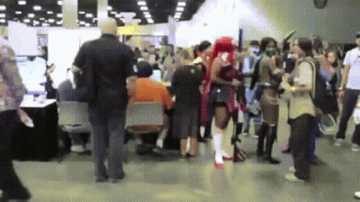 A Crowd Of People Are Gathered In A Room With A Man In An Orange Shirt Sitting At A Table GIF