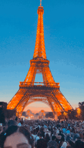 A Crowd Of People Are Gathered In Front Of The Eiffel Tower At Night GIF
